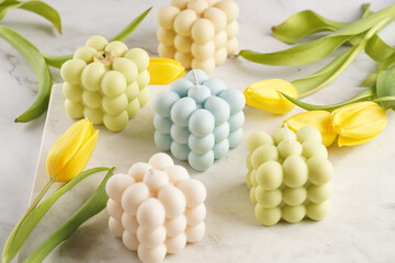Many bubble candles - off-white, beige-colored and blue - on marble board with spring flowers tulips