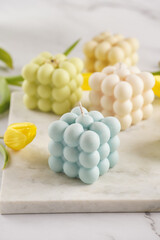 Many bubble candles - off-white, beige-colored and blue - on marble board with spring flowers tulips