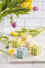 Many bubble candles - off-white, beige-colored and blue - on marble board with spring flowers tulips