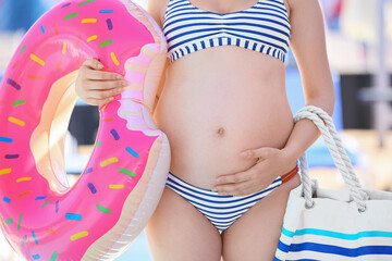 Pregnant woman with inflatable ring and bag near swimming pool