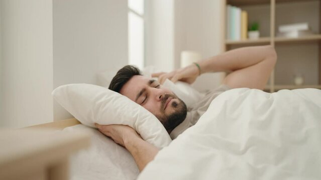 Young hispanic man lying on bed suffering insomnia for noise at bedroom