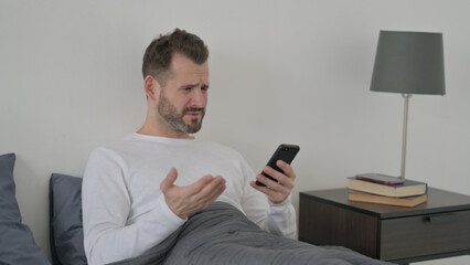 Man Reacting to Loss on Smartphone in Bed