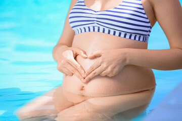 Fototapeta na wymiar Pregnant woman making heart shape on her belly with hands in swimming pool