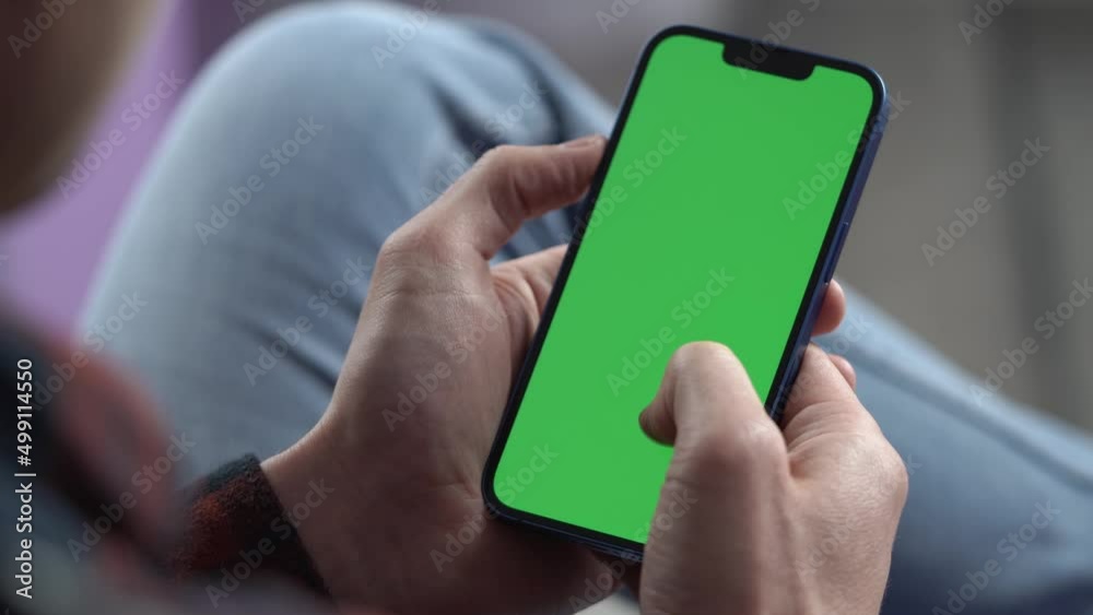 Wall mural man using smartphone in vertical mode with green mock-up screen, doing swiping, scrolling gestures. 