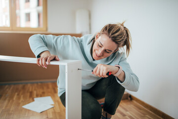 Woman using screwdriver for assembling furniture at home   - obrazy, fototapety, plakaty