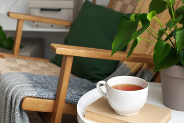Cup of tasty tea with book on table in room
