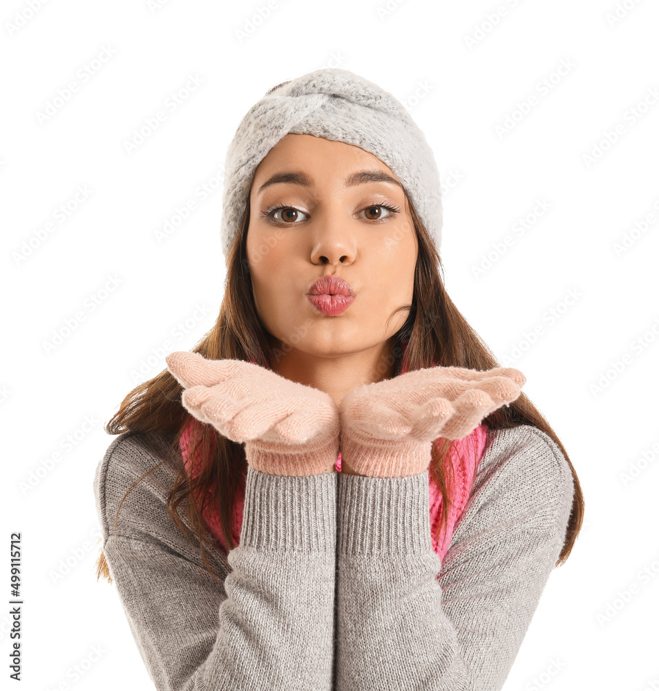 Wall mural Young woman in warm gloves blowing kiss on white background