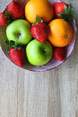 Naklejka na ściany i meble Pink bowl filled with fresh apples, oranges and strawberries on wooden table. Flat lay.