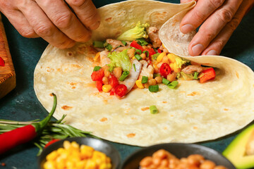 Man preparing tasty burrito with meat on table, closeup