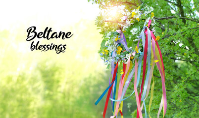Beltane blessings. Flower wreath with colorful ribbons in garden, green natural background. floral...