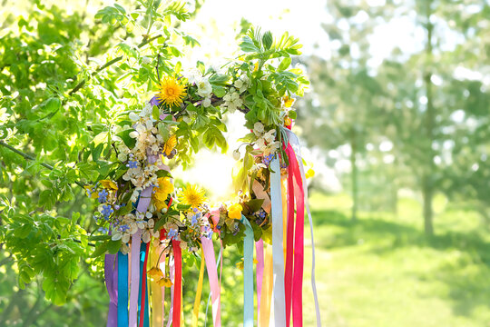 Spring flower wreath with colorful ribbons in garden, green natural background. floral decor, Symbol of Beltane, Wiccan Celtic Holiday beginning of summer season. pagan witch traditions, rituals.