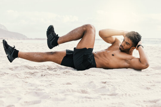 Im working on that six-pack. Shot of a sporty young man doing crunches while at the beach for a workout.