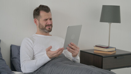 Man Reacting to Loss on Tablet in Bed