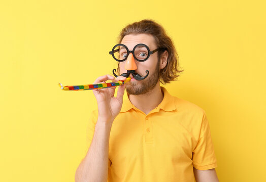 Funny young man in disguise and with party whistle on yellow background. April fools' day celebration