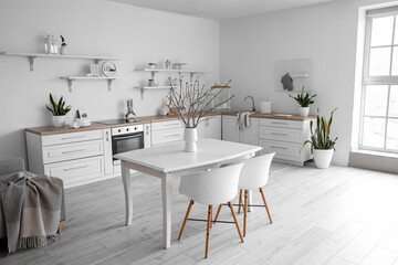 Vase with tree branches on dining table in kitchen interior
