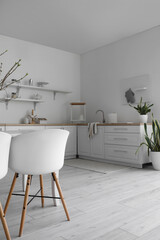 Chairs, modern counters and shelves with kitchenware near white wall in room interior