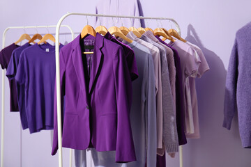Racks with clothes in purple shades on lilac background