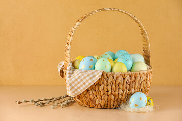 Wicker basket of painted Easter eggs on color background