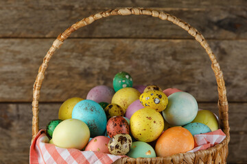 Wicker basket of painted Easter eggs on wooden background, closeup