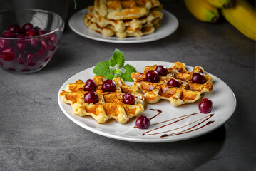 Belgian or Brussels waffles with frozen cherries. Homemade cottage cheese banana waffle in a plate on a dark table