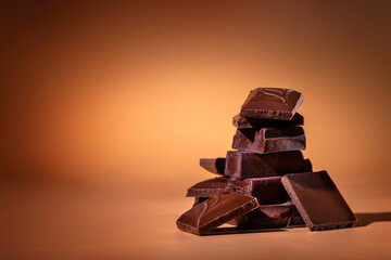 A stack of dark broken chocolate on a bright orange background. Copy space