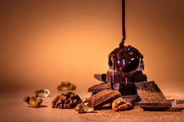 A stack of dark broken chocolate drizzled with melted chocolate and walnuts on a bright orange...