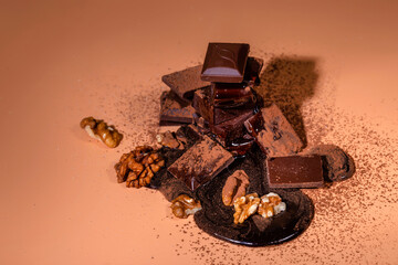A stack of dark broken chocolate drizzled with melted chocolate and walnuts on a bright orange background. Copy space