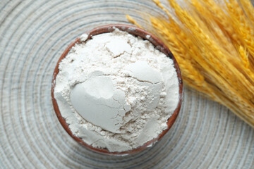 wheat flour in a bowl and wheat ears on table 