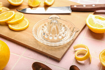 Wooden board with juicer and ripe lemons on color tile