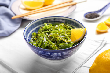Bowl with healthy seaweed salad and lemon on light wooden background