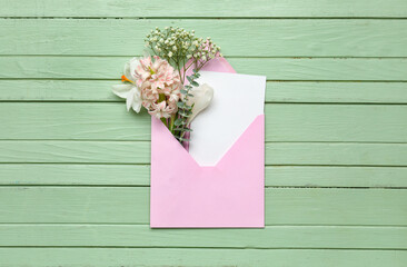 Envelope with card and flowers on green wooden background