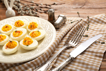Plate with stuffed eggs, cutlery, napkin, willow branches and Easter rabbit on wooden background