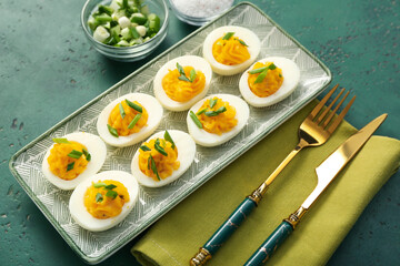 Plate with stuffed eggs, green onion, salt, cutlery and napkin on green background. Easter celebration