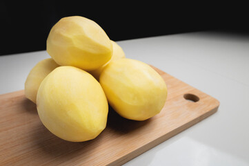 Some peeled potatoes on a wooden cutting board. On a white table against a dark background