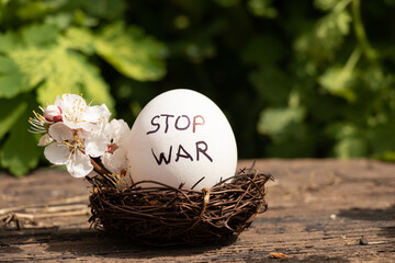 Stop war is written on a white chicken egg that lies in a straw basket in the sun on a farm, peace...