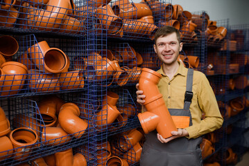 young happy smiling salesman seller/shop assistant is choosing the sewer pipes  in a construction store..