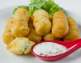 Baked cheese pies on a white bowl with fresh green lettuce leaves.