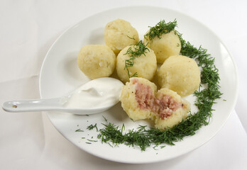 Potato dumplings stuffed with meat, dill and sour cream in a spoon on a white plate.