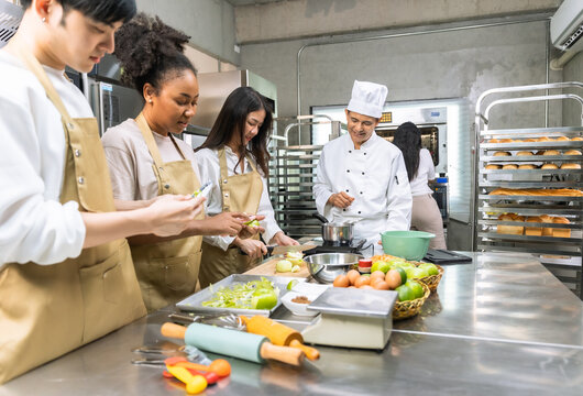 Cooking  course , senior Asian male chef in cook uniform teaches young asian and african american people cooking class students to prepare, mix ingredients for  foods, fruit pies in   kitchen.