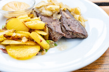 Calf liver served with braised onions and roasted potatoes on a white plate and apple puree in a small glass bowl, copy space, selected focus