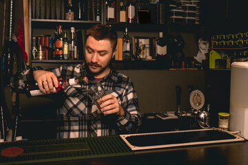 Bartender preparing cocktail behind bar counter, pouring berry liquor into glass