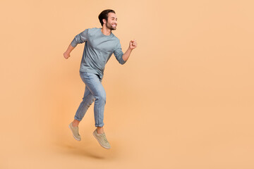Fototapeta na wymiar Full size profile side photo of young cheerful guy runner jumper rush fast isolated over beige color background