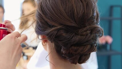 The hairdresser fixes a curl of hair to a brunette girl with varnish close-up. The master does hair styling to a young woman. Business concept, barbershop. Beauty salon, warm light. UHD 4K.