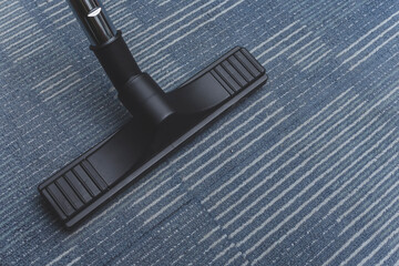 A Floor Carpet Brush Nozzle attachment attached to a vacuum cleaner. Cleaning the blue carpeting.