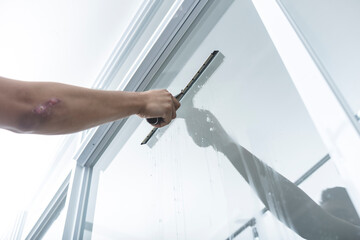 A man cleans the surface of an interior office window with a glass wiper or squeegee. The surface...
