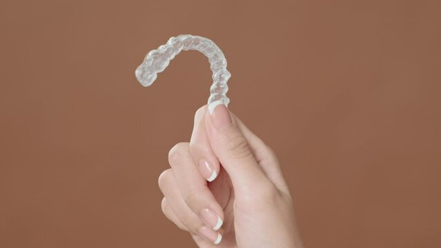 Close up young woman hand is holding Invisalign over brown background
