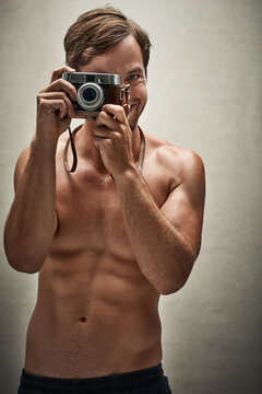 Dont you wish he was taking your picture. Studio shot of a shirtless young man taking photos with a vintage camera.
