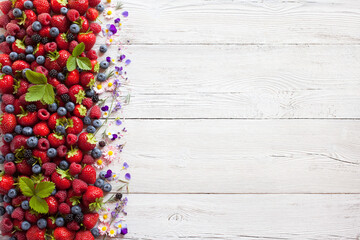 Summer berries strawberries, raspberries, blueberries, blackberries and flowers on a white wooden...