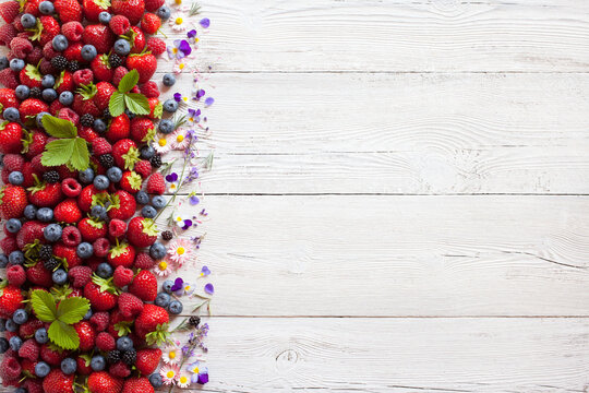 Summer berries strawberries, raspberries, blueberries, blackberries and flowers on a white wooden background, space for text