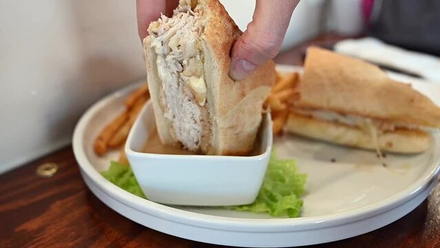 Caucasian female hand dipping turkey sandwich in au jus during lunch, slowmo